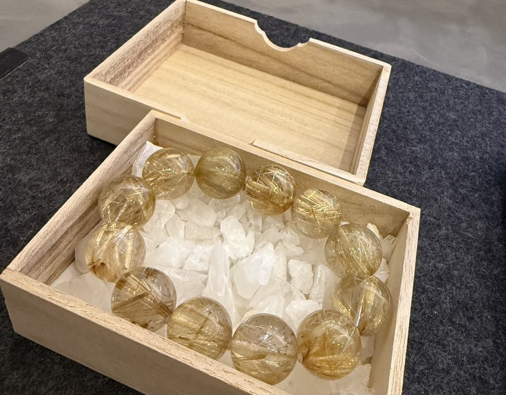 桐箱に水晶のさざれを敷いて納められた、ゴールドルチルクォーツのブレスレット